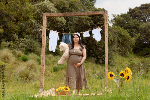 Full Shot of Pregnant Hispanic Woman Standing with Teddy Bear in Meadow Setup