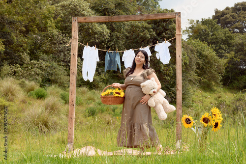 Full Shot of Pregnant Hispanic Woman Standing with Teddy Bear and Sunflower Basket