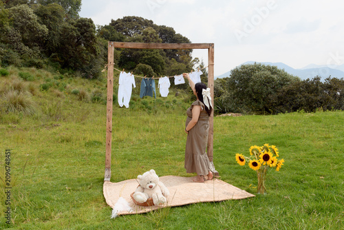 Maternity Photo of Pregnant Woman by Baby Clothes Clothesline in Meadow