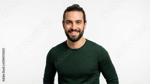 Happy young man with a beard and hair bun wearing a green sweater smiling at the camera on a plain white background