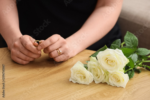 Fotografie Womans hands holding a wedding ring with white roses on a wooden table, loss and