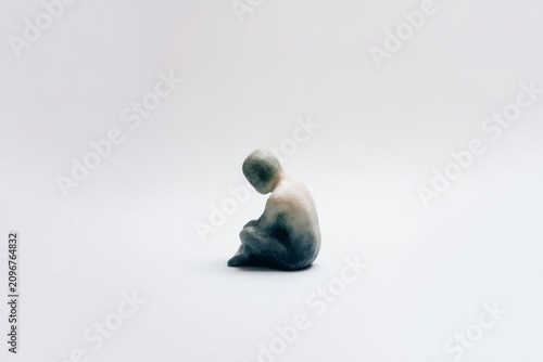 Minimal isolated small seated figure with lowered head on white background for emotional minimalist wallpaper and poster design