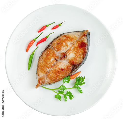 Fried king mackerel fish steak served on a white ceramic plate with fresh red chili peppers and coriander garnish Isolated. Top view of a healthy and tasty seafood meal.