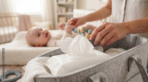 Closeup of a mother preparing to change her babys diaper, reaching for baby wipes from a felt organizer basket in a nursery