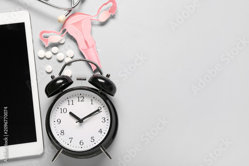 Alarm clock with pills, paper uterus and tablet computer on light background....
