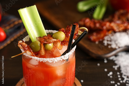 Fotografie Glass of bloody mary cocktail with bacon, olives and celery on wooden background