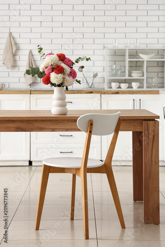 Vase with beautiful dahlia flowers on wooden table in stylish light kitchen