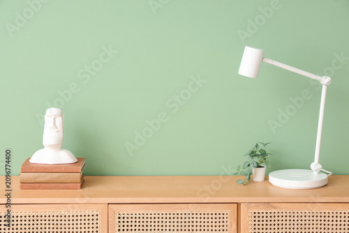 Принти на полотні Modern desk lamp, houseplant, statuette and books on chest of drawers near green