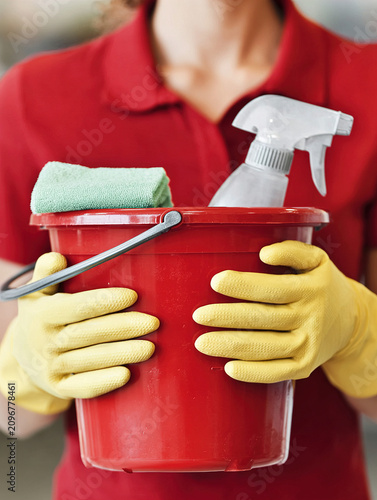 House Cleaner Holding Red Bucket With Spray Bottle, Microfiber Cloth And Yellow Gloves