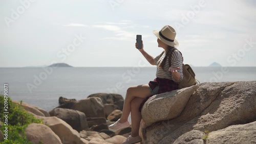 Woman is sitting on a rock and using video call