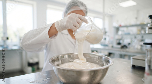 Scientist pouring a thick white substance from a beaker into a metal bowl in a laboratory setting
