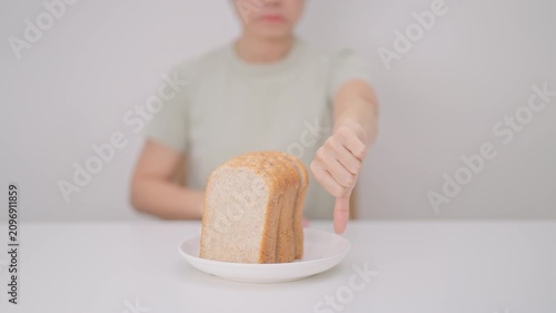 Unhappy woman showing thumbs down gesture and refusing to eat bread. concept of gluten intolerance, gluten sensitivity, carb loading concerns, or a disliking for unhealthy dietary habits