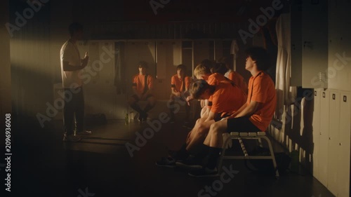 After Match Loss, Coach Addresses Dejected Team Athletes in Locker Room. Players Scattered and Despondent. Man Feedback, Delivered With Supportive Gestures, Aims to Build Character, Set New Goals.