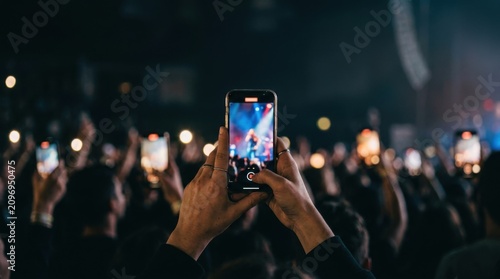 Crowd of concert fans holding up smartphone devices filming live performance music festival stage show