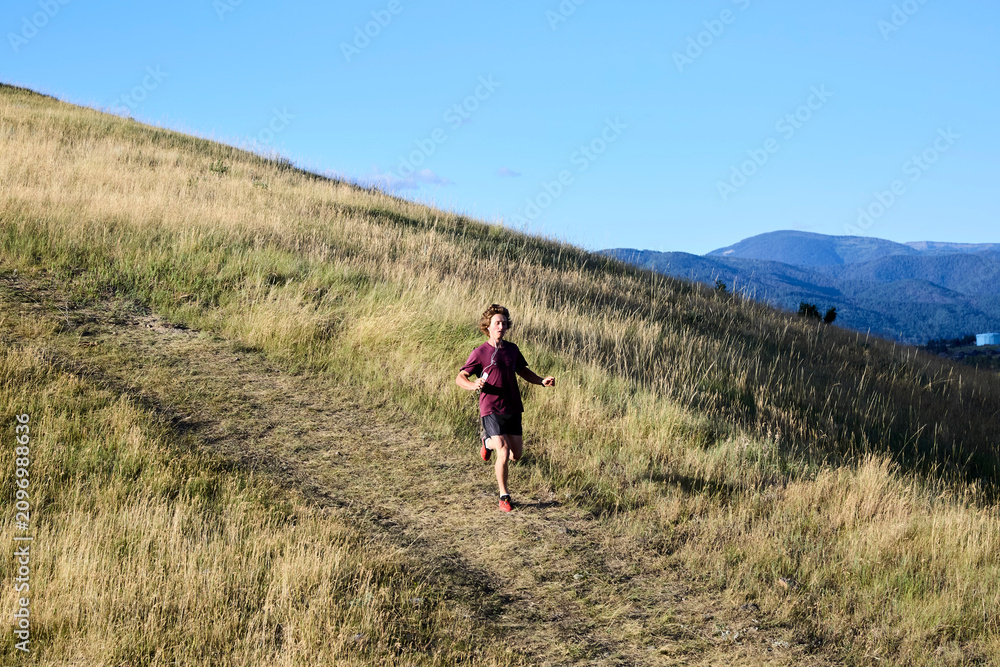 Obraz premium Young man running up grassy hill trail