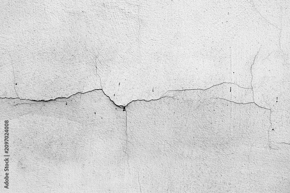 Fototapeta premium Cracked white wall surface detail with rough texture and linear fissures.