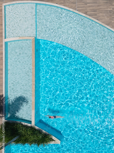 Young girl swimming in clear blue pool during sunny summer vacation. This aerial view captures family,  friends, fun, and recreation at resort, relaxation and joyful outdoor moments.