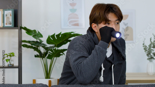 Fotografía Young Man in Hoodie Holding Flashlight While Searching Bright Living Room