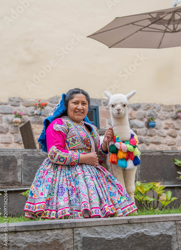 Woman posing with an alpaca in the historic city of Cusco, Peru, surrounded by traditional Andean architecture, showcasing local culture, tourism and the cultural heritage of the Peruvian Andes.