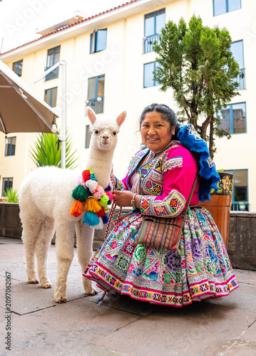 Woman posing with an alpaca in the historic city of Cusco, Peru, surrounded by traditional Andean architecture, showcasing local culture, tourism and the cultural heritage of the Peruvian Andes.