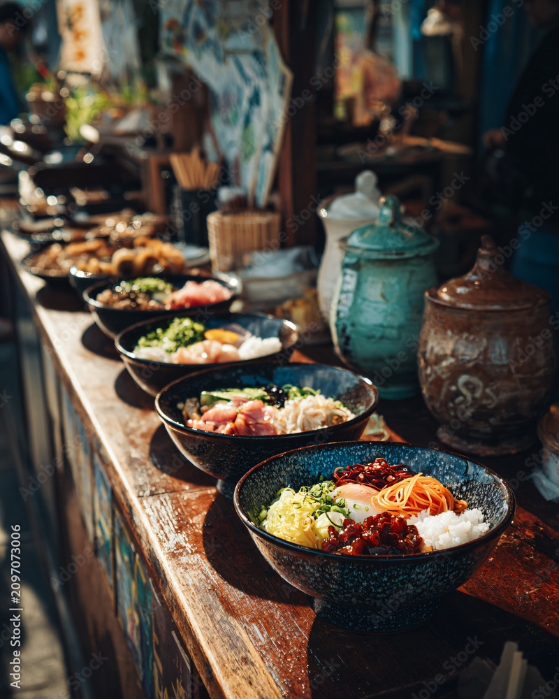 Obraz premium Editorial food photography, freshly prepared Asian rice bowl served at an open-air street market, natural daylight, authentic atmosphere, wooden counter, realistic food styling