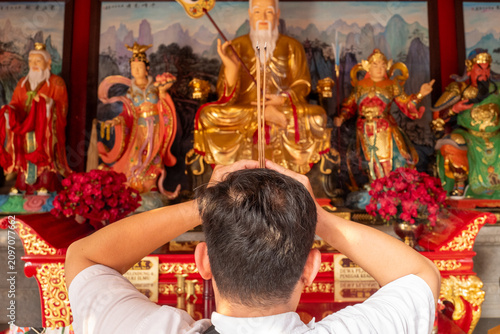 Fotografija Man Praying with Burning Incense Sticks in Front of Deities at a Chinese Temple