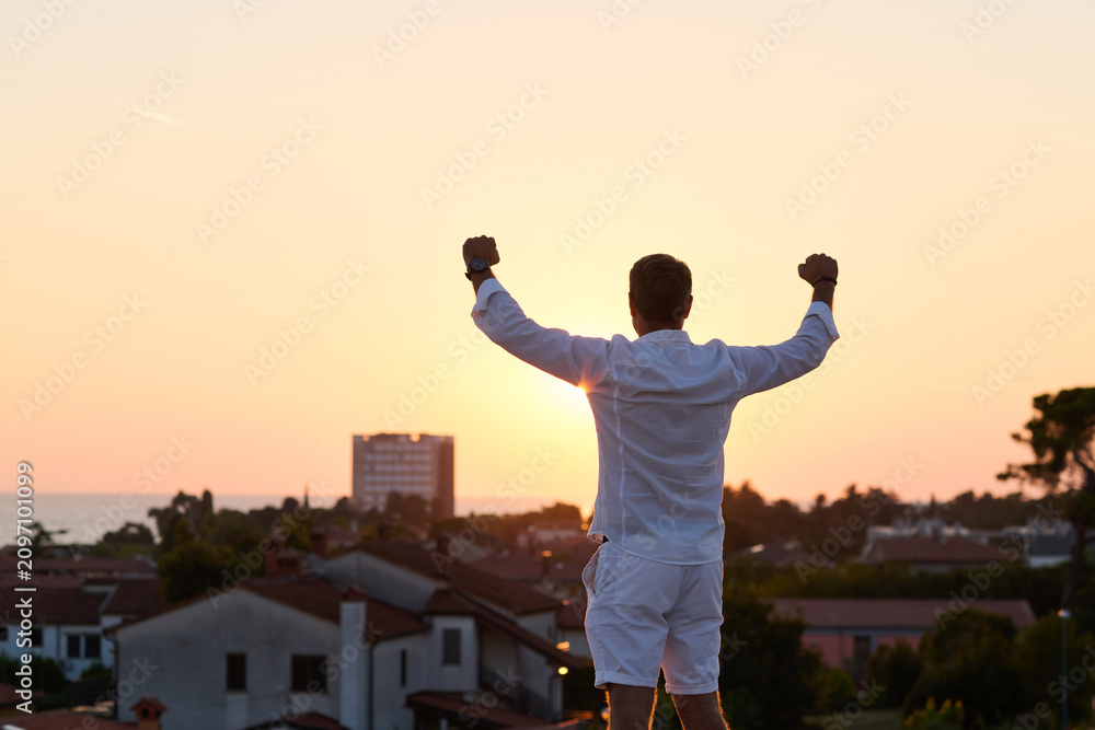 Obraz premium Man Celebrating On Rooftop Terrace At Sunset Over Seaside Town With Balcony View