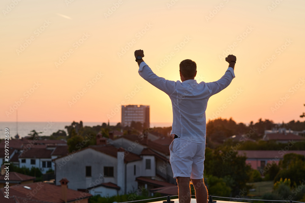 Obraz premium Man Celebrating On Rooftop Terrace Overlooking Sea View At Sunset — Success And Freedom