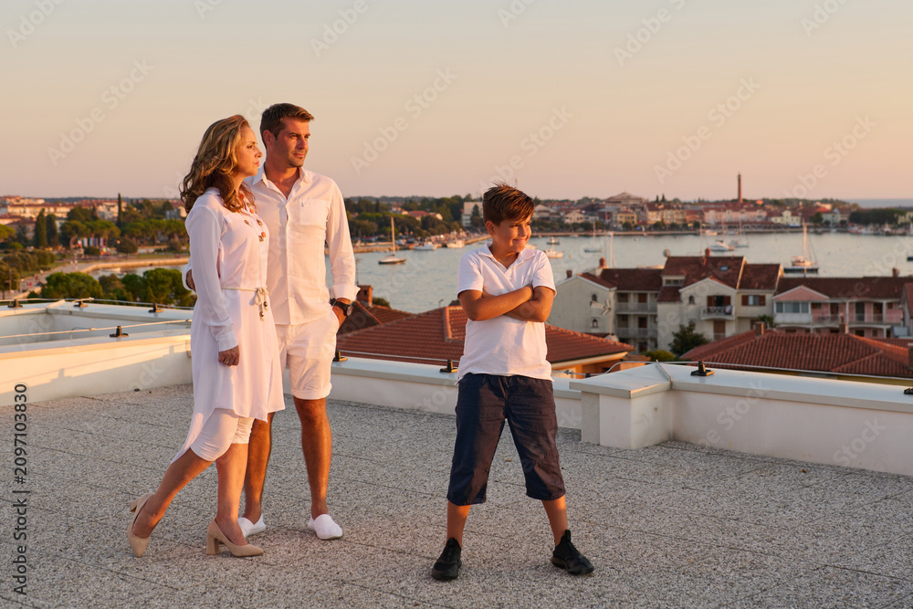 Fototapeta premium Family On Rooftop Terrace With Sea View At Sunset Over Coastal Town
