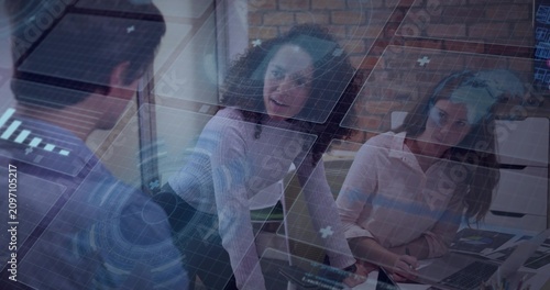 AR HUD appearing, standing woman leaning, gesturing and seated peer scanning laptop, reviewing data