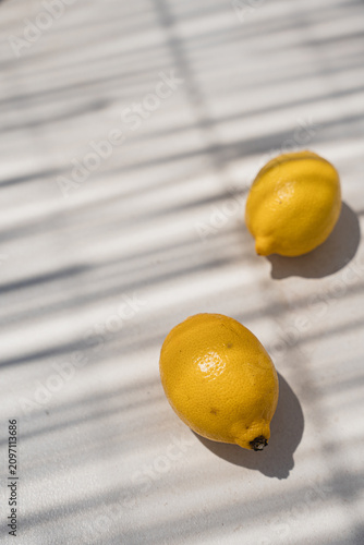 Two Fresh Yellow Lemons On Light Surface With Window Blind Shadows