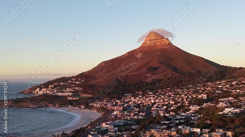Aerial drone view over Camps Bay, Cape Town, at sunset. The Atlantic coastline, golden evening light and Lion's Head in the background create one of South Africa's most iconic coastal landscapes.