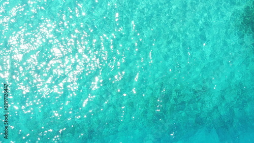 Aerial top down view of turquoise to deep blue sea water texture with sun rays reflection