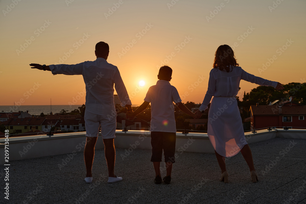 Obraz premium Family Holding Hands on Rooftop Terrace at Sunset With Sea View and Silhouettes