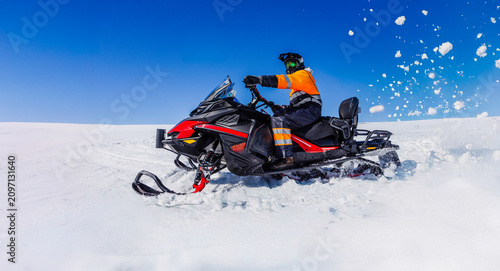 Obraz na plátně Snowmobile rider racing across a pristine Icelandic glacier, sending fresh snow into the air beneath a vivid blue sky