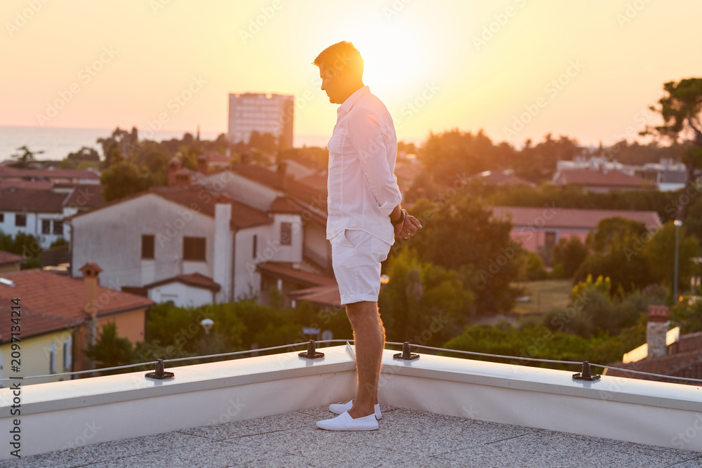 Obraz premium Man Standing On Rooftop Balcony At Sunset Overlooking Sea View And Coastal Town For Vacation