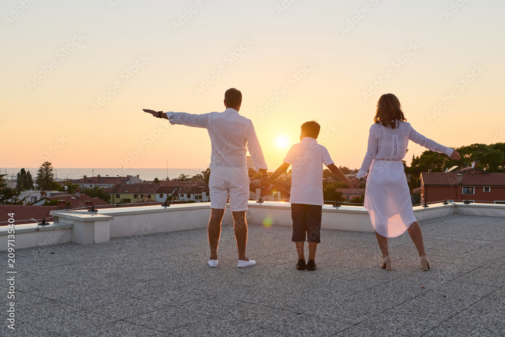 Obraz premium Family Holding Hands on Rooftop Terrace at Sunset With Sea View and Summer Vibes
