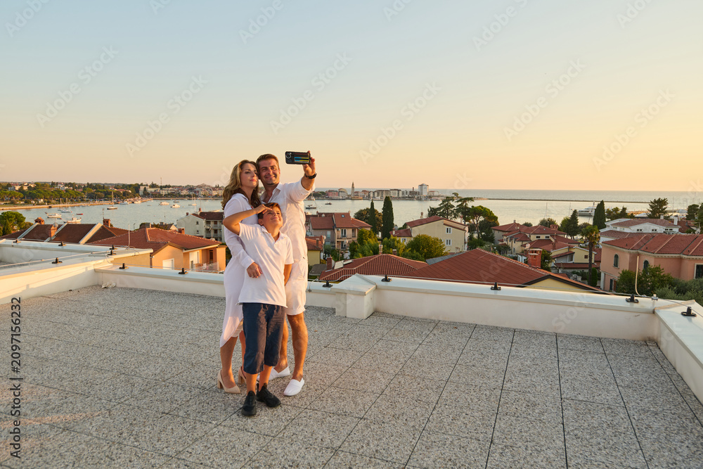 Obraz premium Family Taking Selfie On Rooftop Terrace With Sea View At Sunset During Summer Vacation