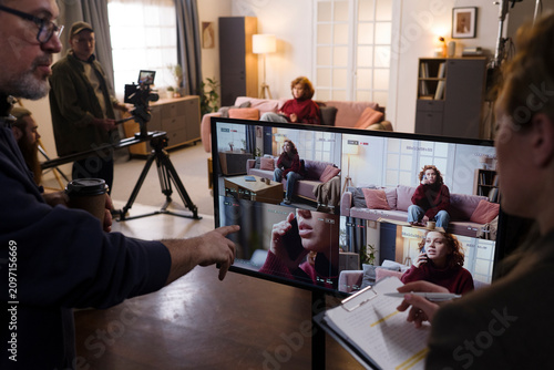Director points at monitor while reviewing playback with film crew
