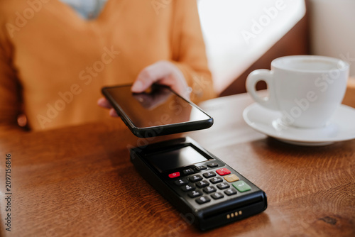 Woman paying through smart phone on credit card reader near coffee cup at table