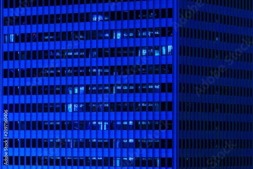 Minimalist abstract view of modern skyscraper facade at night with dense blue lighting and glass windows.