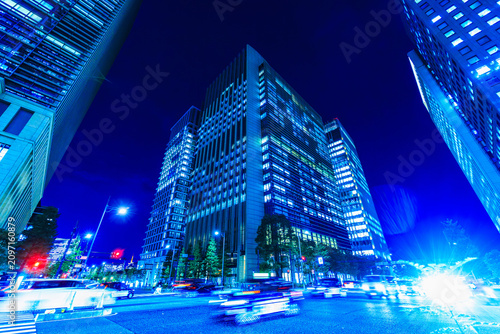 Wide-angle night cityscape of Tokyo financial district with fast-moving traffic light trails and illuminated skyscrapers.