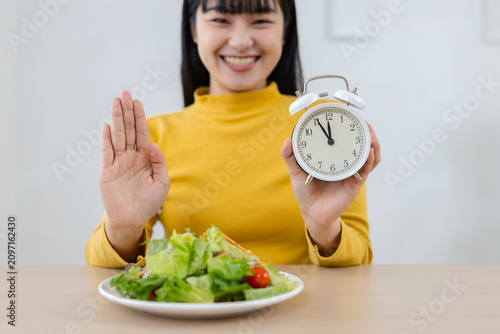 Cuadro en lienzo Happy Asian woman on an intermittent fasting diet holds clock, showing stop gesture