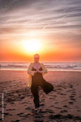 Obraz na plátně Woman standing in the yoga tree pose with palms pressed together at her chest in a gesture of gratitude on the beach at sunset a meditative moment of stillness and focus