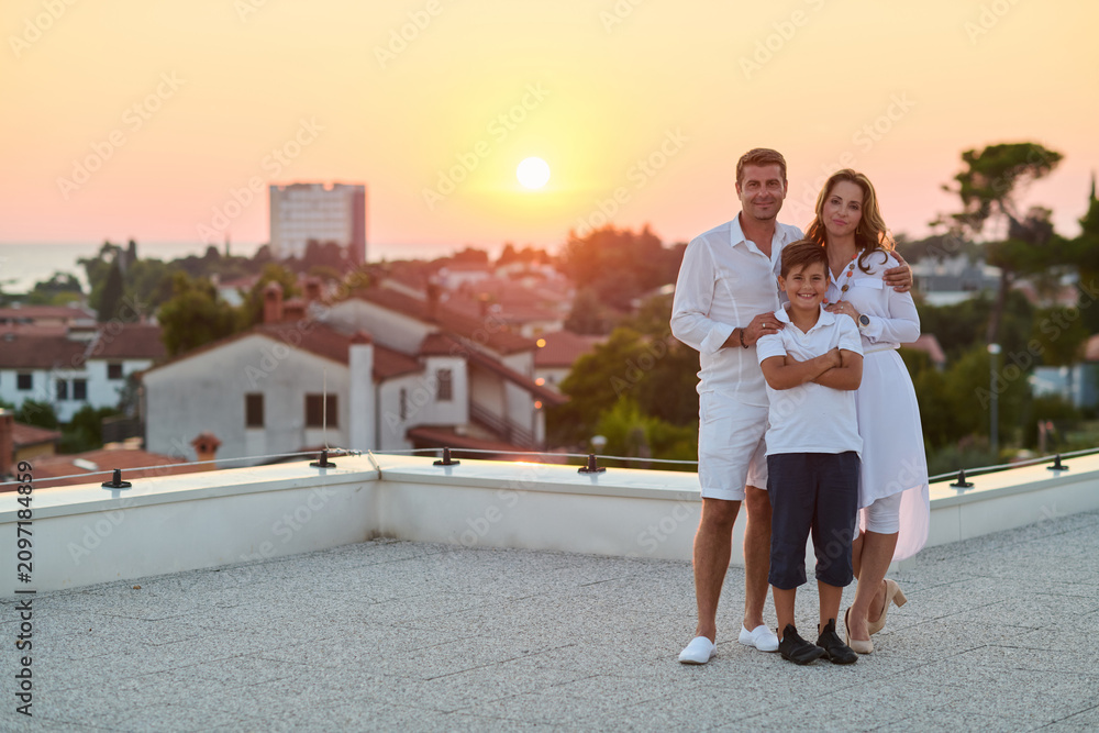 Obraz premium Happy Family On Rooftop Terrace At Sunset With Sea View During Coastal Vacation