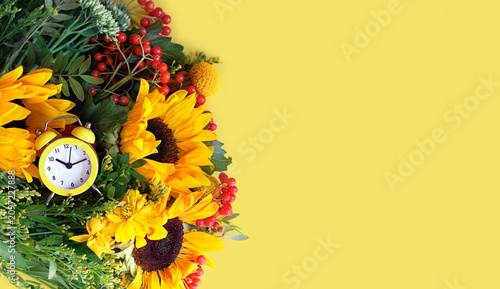Fotografie Bright autumnal flowers bouquet with sunflowers, red berries of viburnum and alarm clock on yellow background