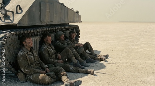 Soldiers resting in the shade of a tank in the desert