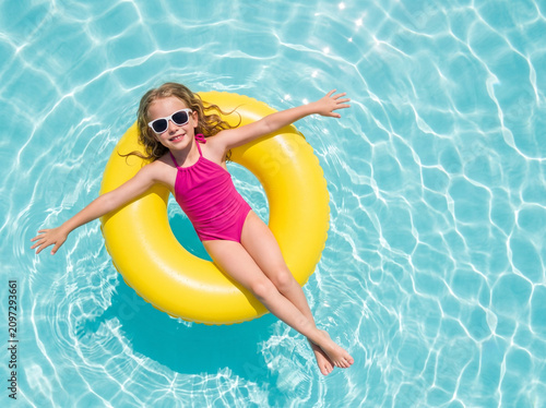 Happy young white girl floating on a bright yellow swim ring in a luxury swimming pool during summer vacation with clean copy space for travel and lifestyle campaigns