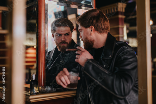 Canvas Print Two friends together sit at a bar mirror, one holding a glass of whiskey and a cigar
