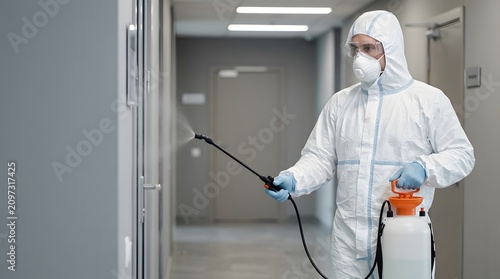 Cleaning specialist in a hazmat suit holding a disinfectant spray